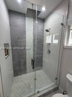 Walk-in shower featuring a frameless glass enclosure, ceiling-mounted rainfall showerhead, pebble stone floor, vertical mosaic tile accent, and a built-in recessed wall niche