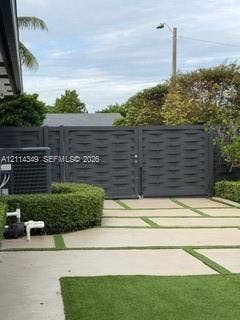 Private driveway featuring concrete pavers with artificial turf inlay, enclosed by a charcoal-finished privacy gate and manicured perimeter hedges