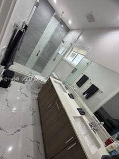 Dual-sink vanity with wood-finish cabinetry, white countertop, and integrated sinks, complemented by floor-to-ceiling tile in the walk-in glass-enclosed shower and large-format tile flooring