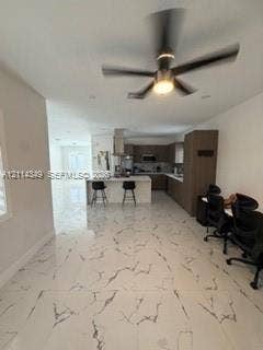 Large-format tile flooring with veining detail, central island with seating, stainless steel range hood, built-in cabinetry, and ceiling-mounted light fixture with fan