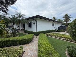 Single-story exterior featuring white stucco finish, dark-toned hip roof, stone-paver walkways, and manicured shrubbery