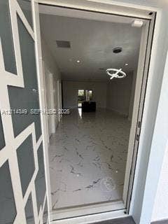 Entryway featuring a glass door with a geometric overlay, large-format tile flooring with veining detail, recessed ceiling lighting, and a modern sculptural pendant fixture