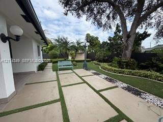 Backyard featuring large-format paver hardscaping with turf ribbons, mature specimen trees, sculpted landscaping, and wall-mounted exterior globe lighting