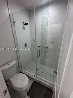 Walk-in shower featuring a frameless glass enclosure, pebble-stone flooring, a decorative vertical glass tile accent, and a wall-mounted showerhead
