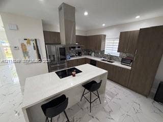 Kitchen featuring a central island with a quartz countertop and integrated cooktop, stainless steel chimney-style range hood, wood-finish cabinetry, stone-tile backsplash, and polished stone-finish flooring