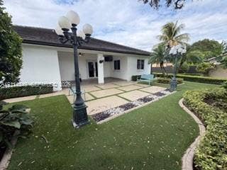 Covered concrete patio with geometric inlay, manicured lawn, established shrubbery, and multi-globe ornamental lamp posts