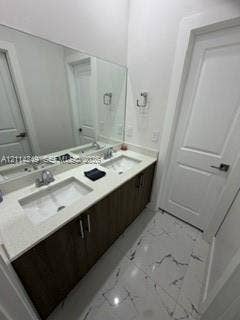 Double-sink vanity featuring dark wood-finish cabinetry, light-toned stone-finish countertop, undermount sinks, and polished chrome fixtures, complemented by large-format marbled tile flooring