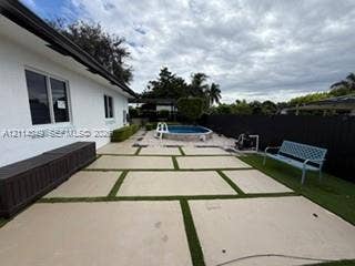 Outdoor patio featuring large-format concrete pavers with turf inlay, above-ground pool with stone-finish surround, and perimeter privacy fencing