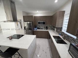 Kitchen featuring wood-finish cabinetry, quartz countertops, a central island with a built-in cooktop, stainless steel chimney-style range hood, and tile flooring