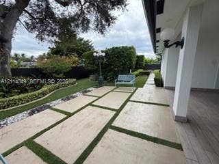 Covered patio featuring wood-finish flooring, large-format concrete pavers with turf inlays, professional landscaping, and wall-mounted exterior lighting