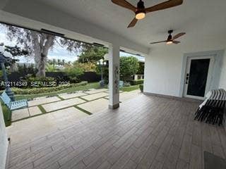 Covered patio featuring wood-finish tile flooring, dual ceiling fans, and an outdoor living area with stone paver hardscaping and integrated turf