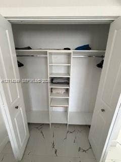 Walk-in closet featuring white-finish built-in shelving, two overhead storage ledges, metal hanging rods, and large-format tile flooring with a veined pattern