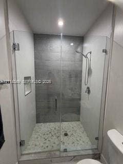 Walk-in shower featuring a glass enclosure, gray tile surround, pebble-style floor, built-in recessed niche, and handheld shower fixture