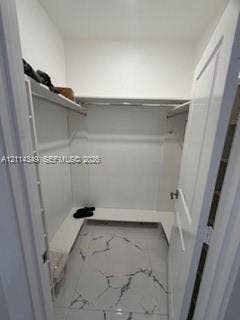 Walk-in storage space featuring white built-in shelving, integrated hanging rods, and large-format porcelain tile flooring with marble-finish veining