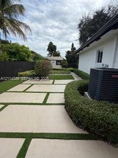 Backyard featuring large-format paver hardscaping with turf ribbons, perimeter privacy fencing, manicured hedges, and an external storage structure