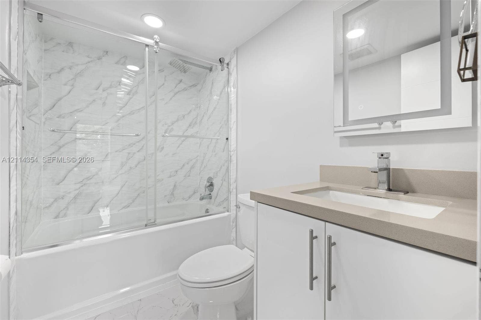 14401 SW 88th Street, #410N, Miami, FL 33186 Bathroom featuring a tub-shower combination with floor-to-ceiling stone-pattern tile, a sliding glass door, a vanity with a solid-surface countertop and integrated sink, and a modern rectangular mirror with perimeter integrated lighting