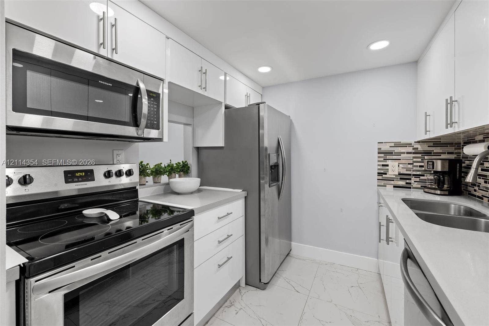14401 SW 88th Street, #410N, Miami, FL 33186 Kitchen featuring white gloss cabinetry, stone-finish countertops, stainless steel appliances, a multi-tone glass tile backsplash, and large-format porcelain tile flooring
