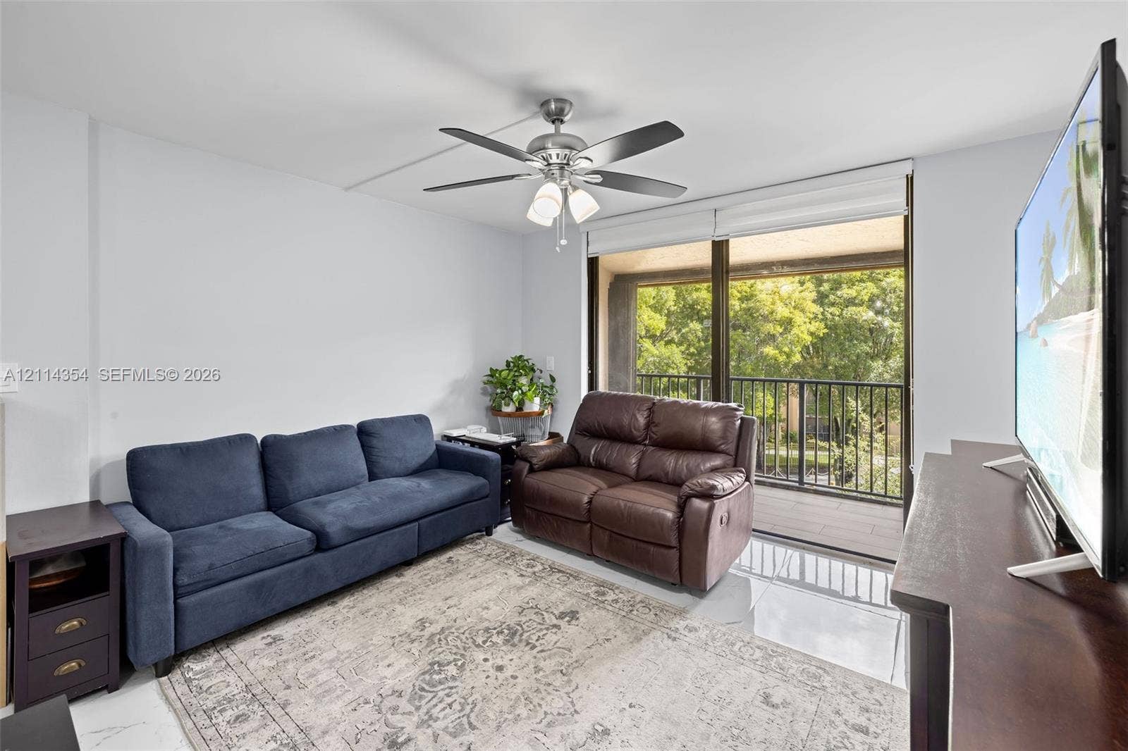 14401 SW 88th Street, #410N, Miami, FL 33186 Living area featuring polished tile flooring, a multi-blade ceiling fan with integrated lighting, and full-width sliding glass doors opening to a balcony with metal railing