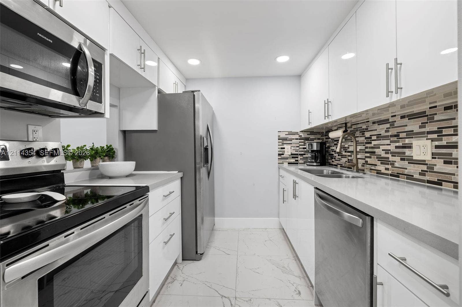 14401 SW 88th Street, #410N, Miami, FL 33186 Kitchen featuring white high-gloss cabinetry, stainless steel appliances, multi-tonal linear tile backsplash, solid-surface countertops, and large-format tile flooring