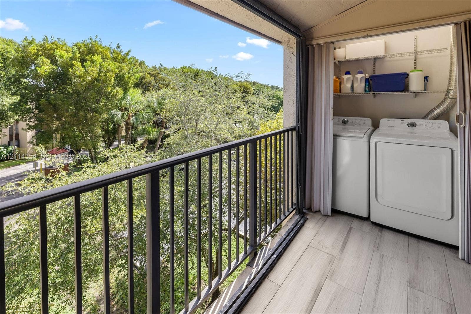 14401 SW 88th Street, #410N, Miami, FL 33186 Balcony featuring black metal railing, wood-finish tile flooring, and integrated laundry area with wire shelving