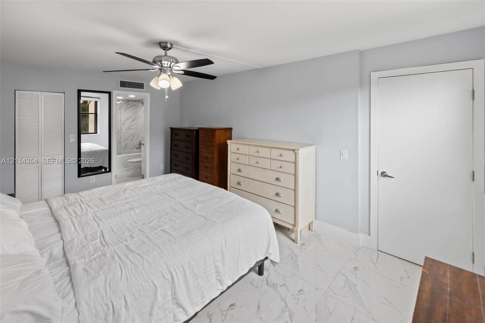 14401 SW 88th Street, #410N, Miami, FL 33186 Interior space featuring stone-style tile flooring, multi-blade ceiling fan with integrated light fixture, dual louvered closet doors, and smooth-finish walls