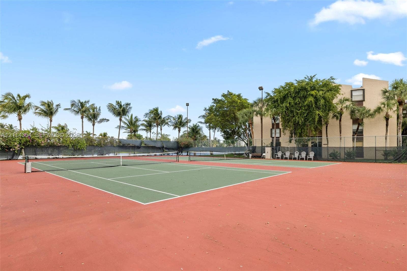 14401 SW 88th Street, #410N, Miami, FL 33186 Hard-court tennis facility featuring perimeter chain-link fencing, dual courts, overhead lighting, and mature palm landscaping