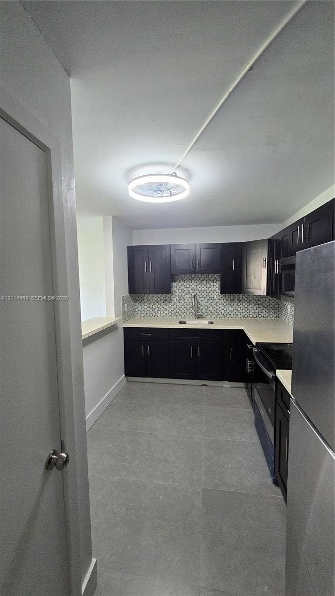 14840 Naranja Lakes Boulevard, #1G, Homestead, FL 33032 Kitchen featuring dark cabinetry, solid-surface countertops, mosaic tile backsplash, stainless steel appliances, and large-format floor tile