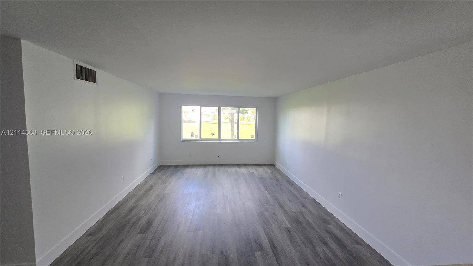 14840 Naranja Lakes Boulevard, #1G, Homestead, FL 33032 Open-concept interior space featuring wood-finish flooring and expansive white walls, illuminated by a multi-pane window