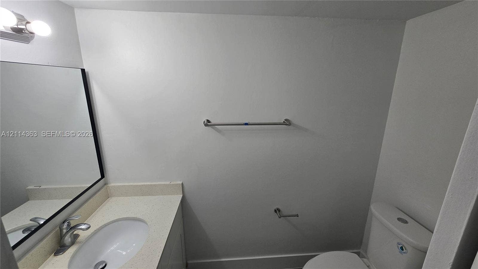 14840 Naranja Lakes Boulevard, #1G, Homestead, FL 33032 Vanity featuring a solid-surface countertop with an integrated oval basin, polished chrome faucet, rectangular mirror with a dark frame, and wall-mounted light fixture