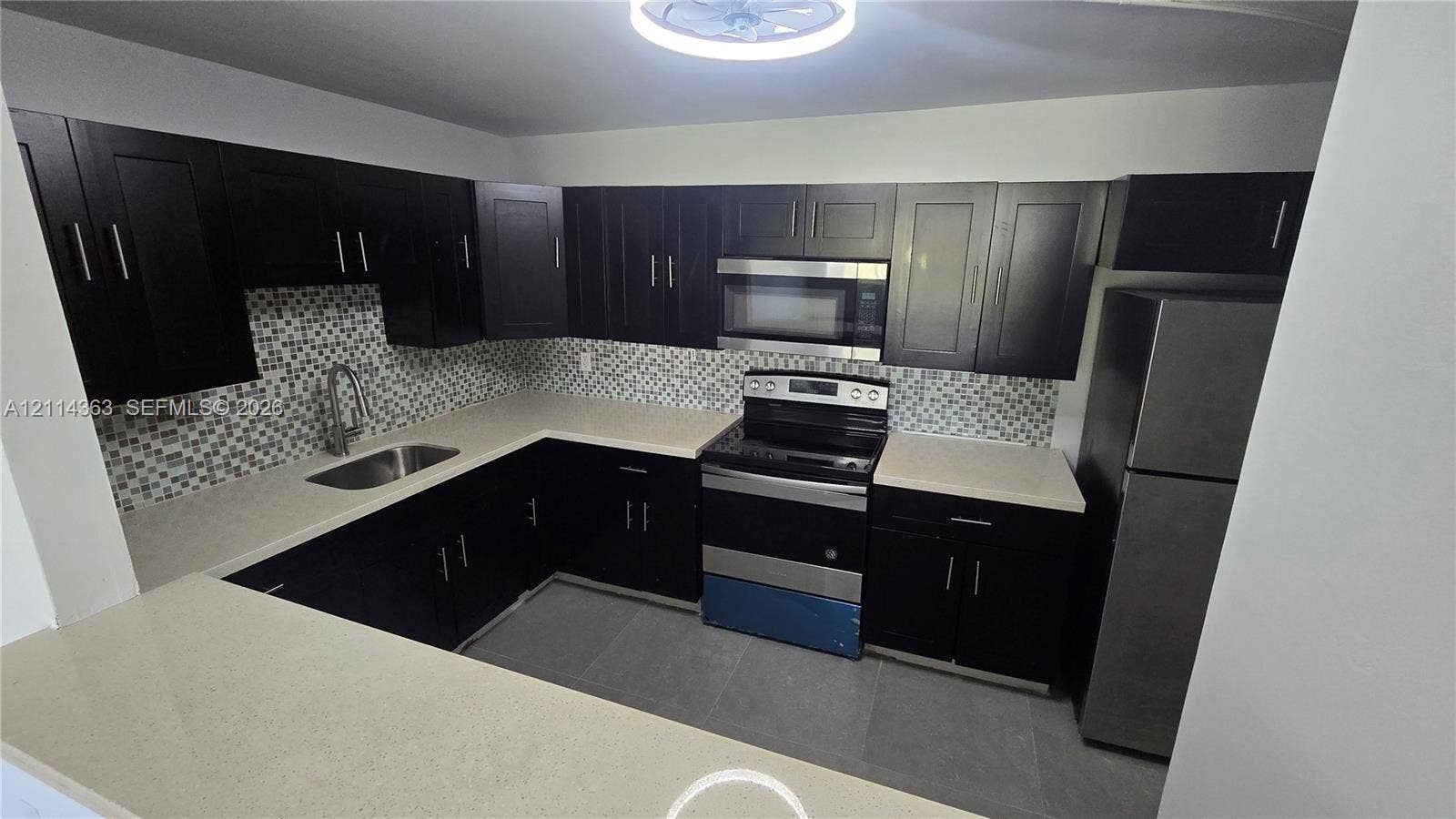 14840 Naranja Lakes Boulevard, #1G, Homestead, FL 33032 Kitchen featuring dark wood-finish cabinetry, light-toned stone countertops, mosaic tile backsplash, stainless steel appliances, and a pass-through breakfast bar