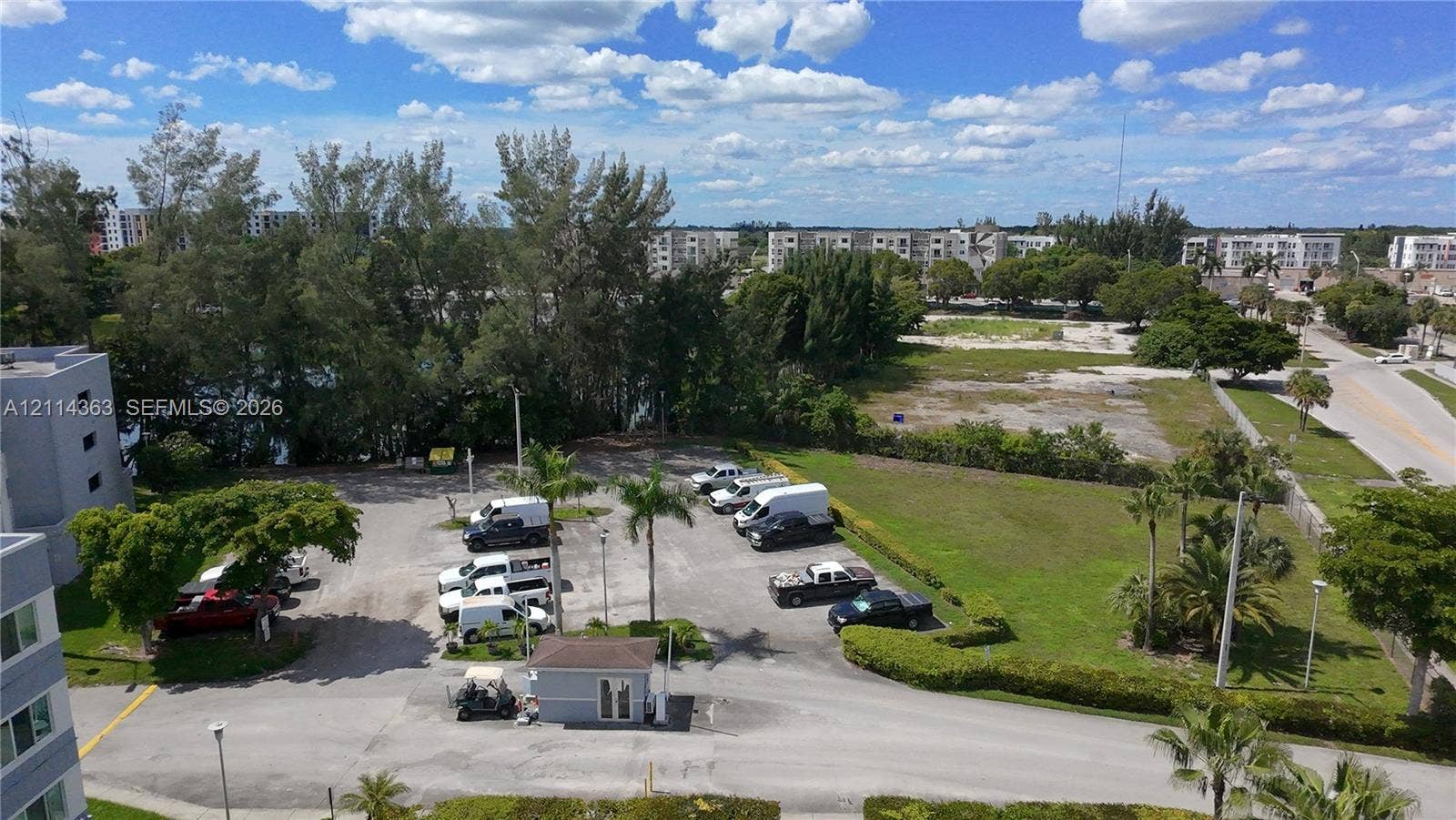 14840 Naranja Lakes Boulevard, #1G, Homestead, FL 33032 Aerial perspective featuring an asphalt parking area, a standalone gated access structure, manicured perimeter landscaping, and mature palm trees