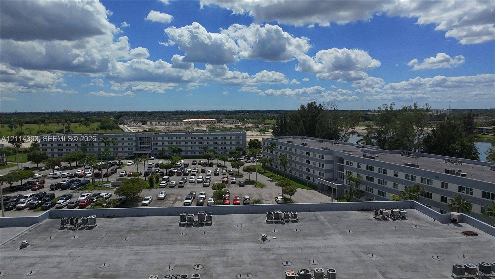 14840 Naranja Lakes Boulevard, #1G, Homestead, FL 33032 Aerial perspective of a multi-story residential building featuring a flat roof with exterior-mounted HVAC units and an expansive asphalt parking lot