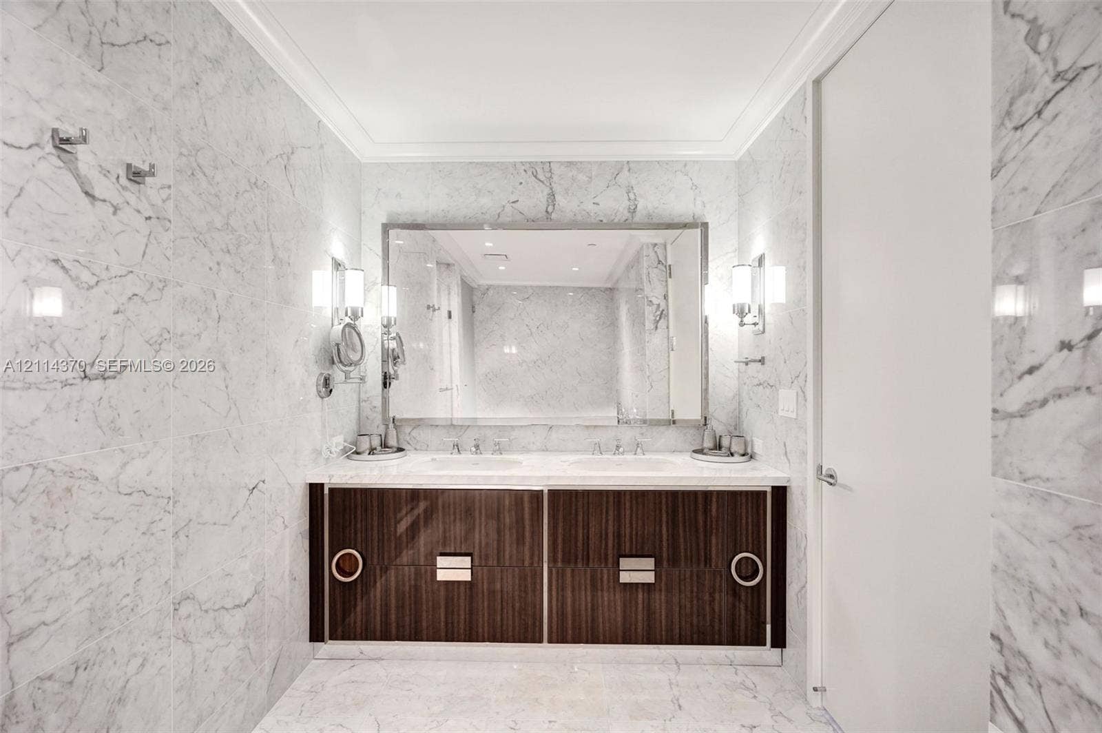 Sunny Isles Beach, Sunny Isles Beach, FL 33160 Double vanity with a stone countertop, dark wood-finish cabinetry, a large rectangular mirror, and wall-mounted metal light fixtures, all encased in full-height stone wall cladding