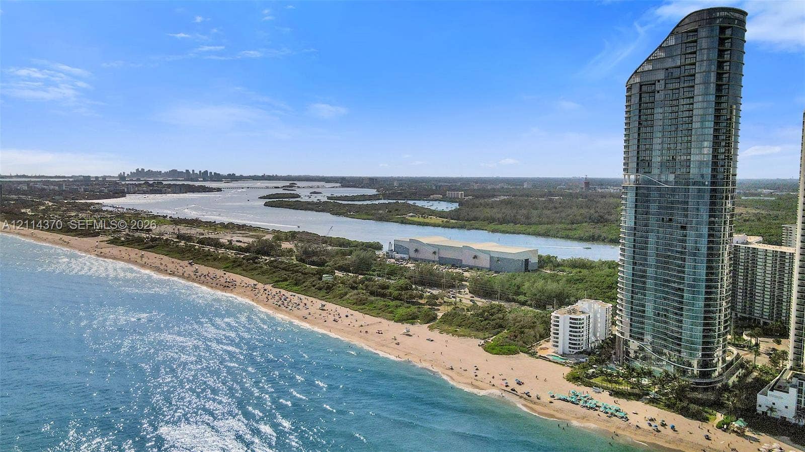 Sunny Isles Beach, Sunny Isles Beach, FL 33160 High-rise architectural exterior featuring a glass-paneled facade, positioned along a coastline with direct sandy beach frontage and proximity to tidal waterways