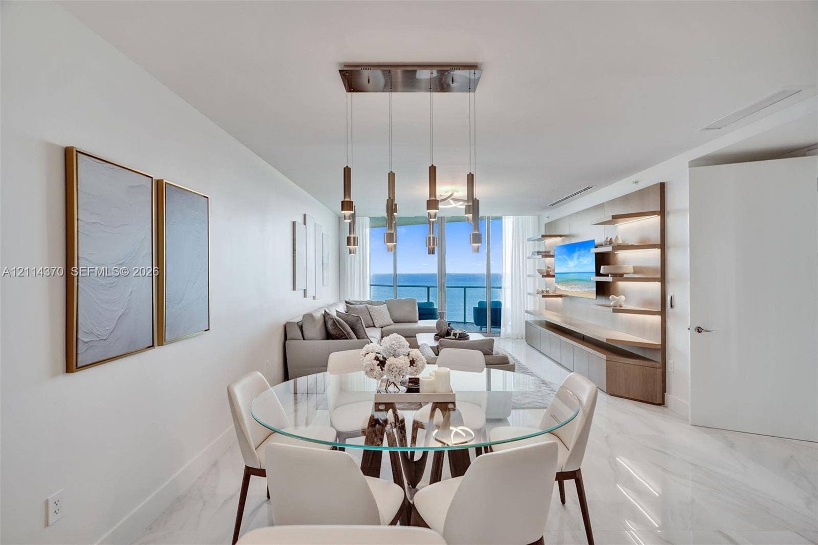 Sunny Isles Beach, Sunny Isles Beach, FL 33160 Large-format polished stone flooring, custom integrated cabinetry with illuminated shelving, multi-pendant rectangular lighting fixture, floor-to-ceiling glass paneling, and ocean scenery