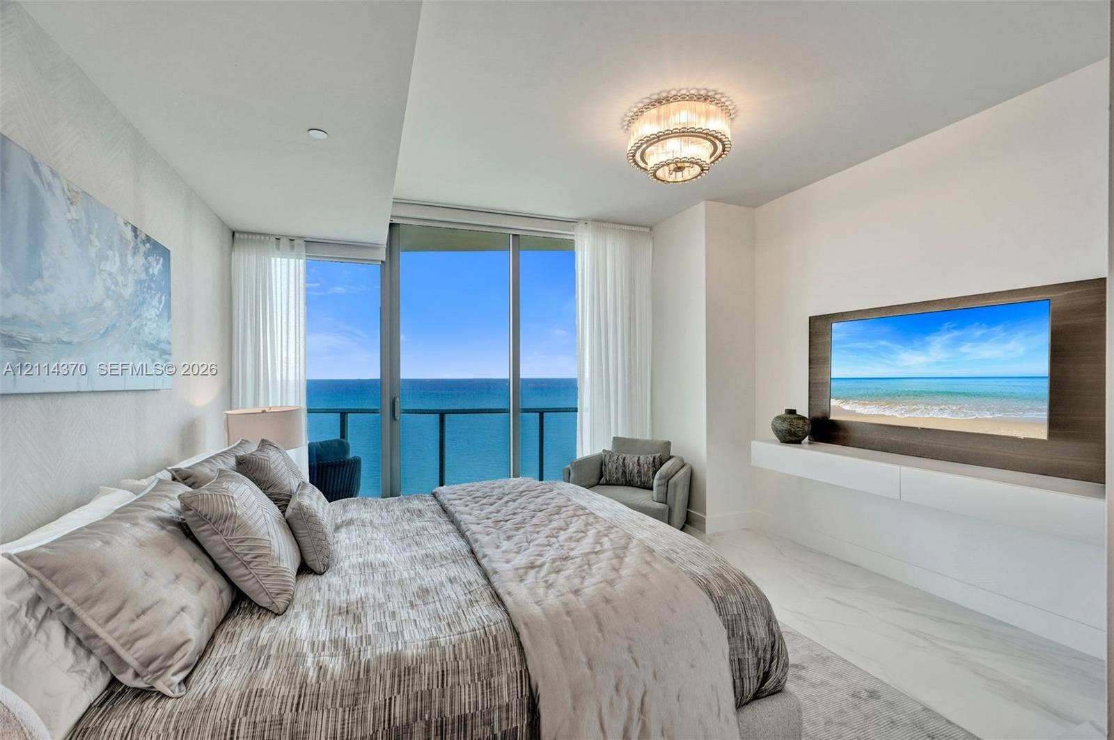 Sunny Isles Beach, Sunny Isles Beach, FL 33160 Floor-to-ceiling glass sliding doors, wood-finish media wall panel, wall-mounted floating console, stone-finish tile flooring, and tiered crystal flush-mount light fixture