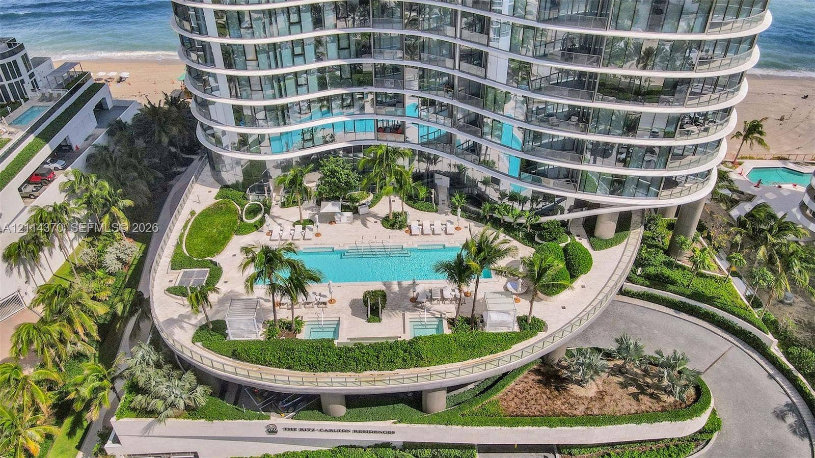 Sunny Isles Beach, Sunny Isles Beach, FL 33160 High-rise tower featuring a curved glass facade, an elevated pool deck with two integrated hot tubs, and meticulously maintained tropical landscaping