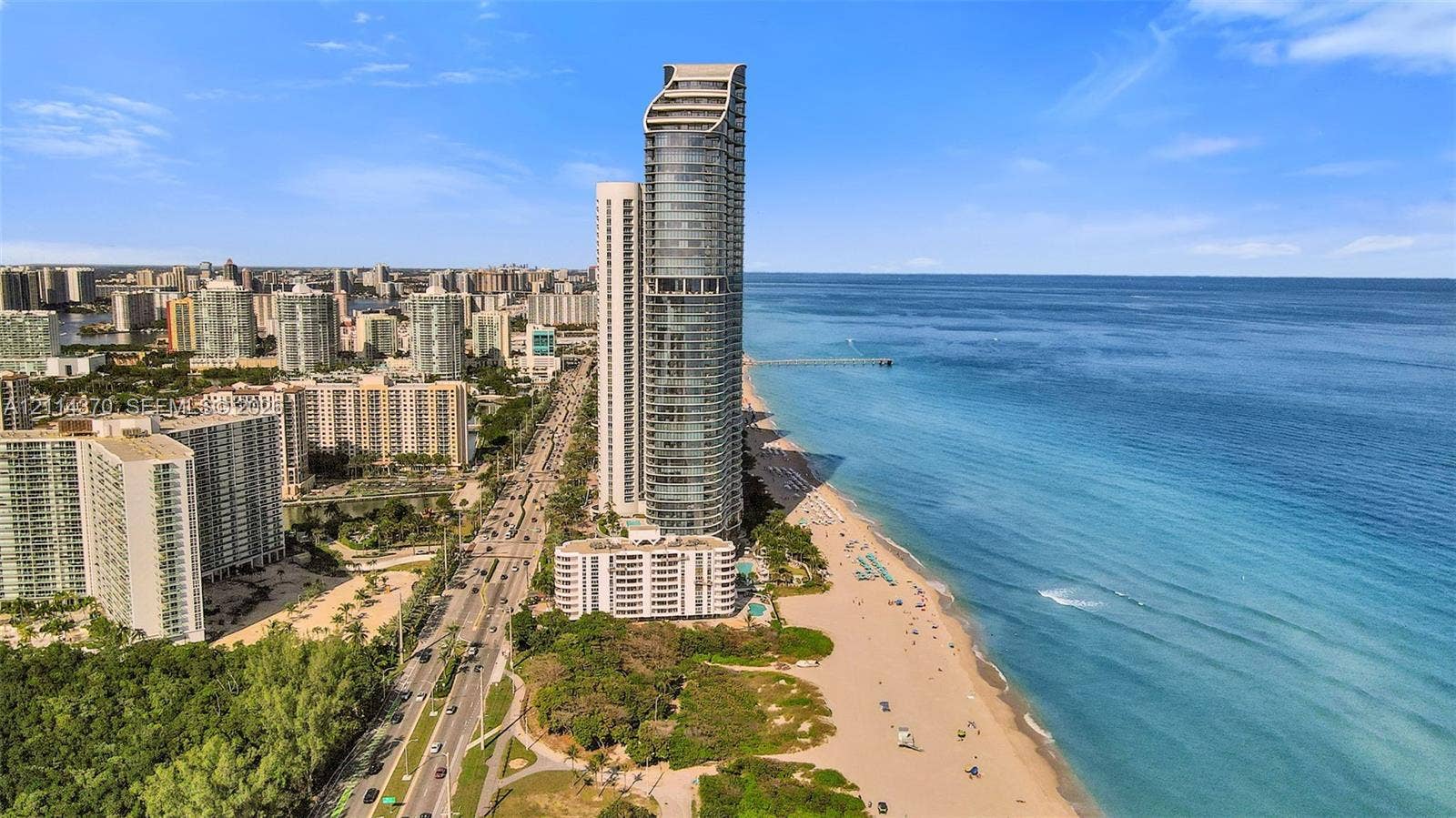 Sunny Isles Beach, Sunny Isles Beach, FL 33160 High-rise residential tower featuring a glass facade, oceanfront positioning, direct beach access, and coastal scenery