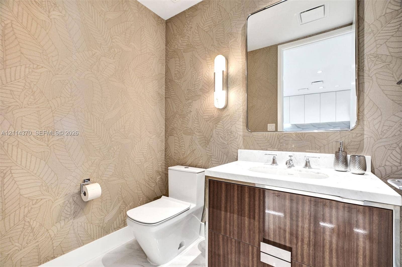 Sunny Isles Beach, Sunny Isles Beach, FL 33160 Wall-mounted vanity featuring wood-finish cabinetry, white countertop, integrated sink, vertical wall-mounted lighting, and patterned wallpaper