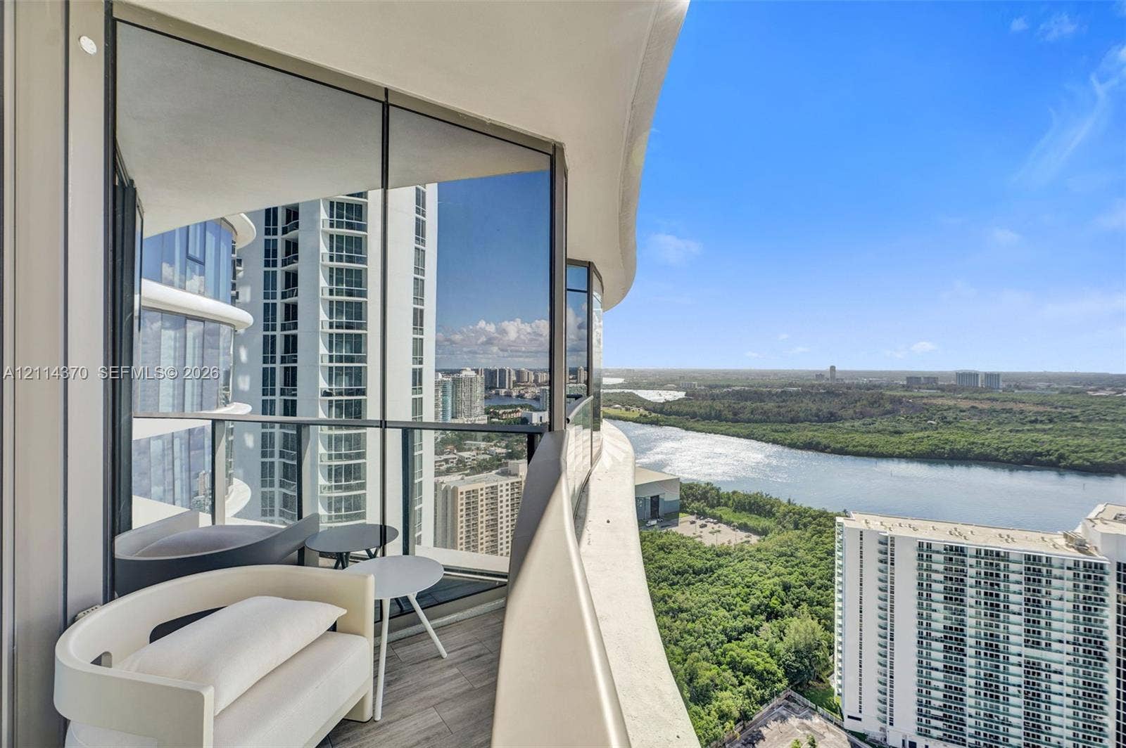 Sunny Isles Beach, Sunny Isles Beach, FL 33160 Curved exterior balcony featuring glass railing, wood-finish flooring, and expansive floor-to-ceiling glass paneling