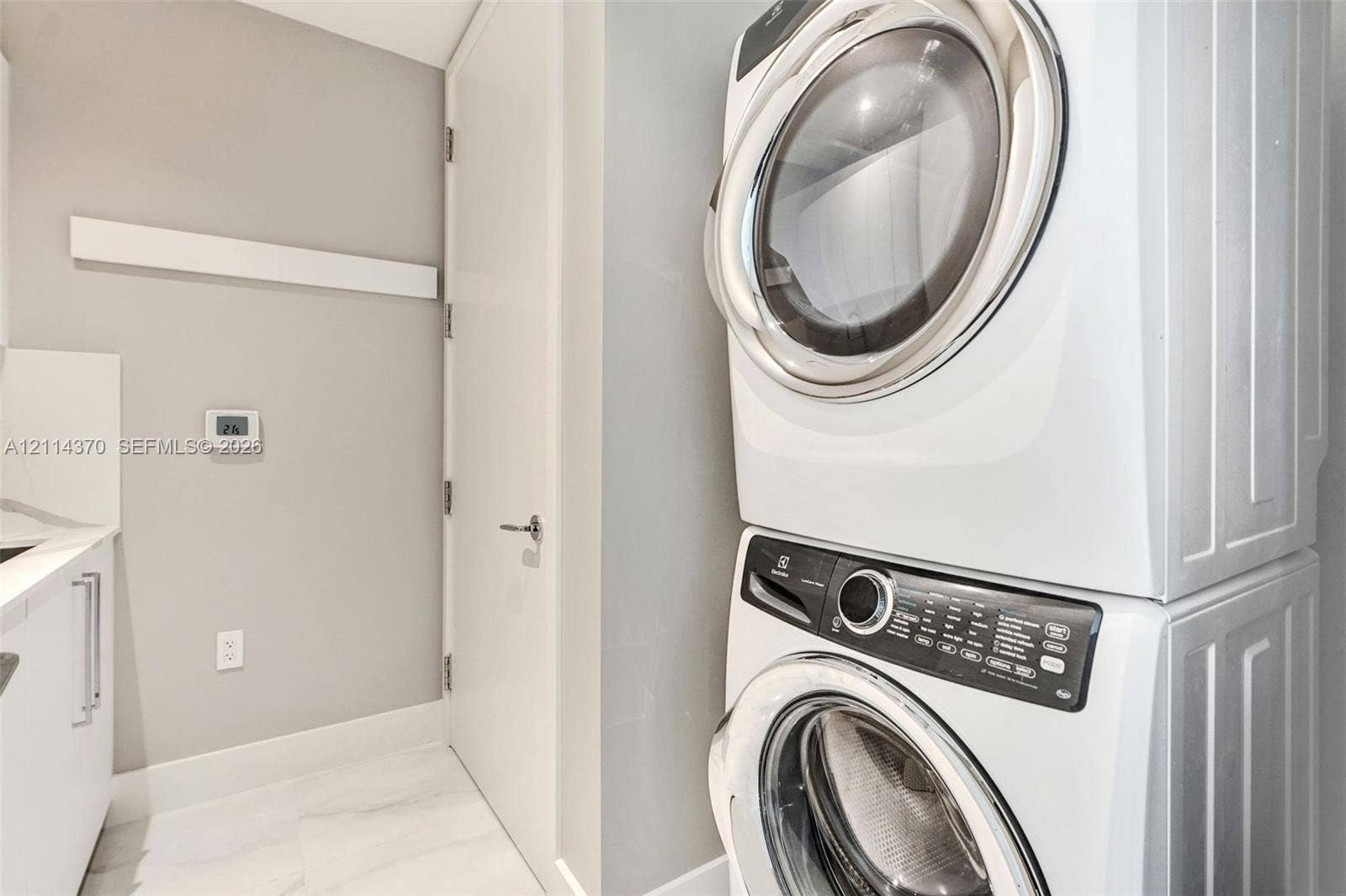 Sunny Isles Beach, Sunny Isles Beach, FL 33160 Laundry area featuring a stacked white front-load washer and dryer, stone-patterned tile flooring, integrated white cabinetry, and a solid-core interior door with modern metal hardware