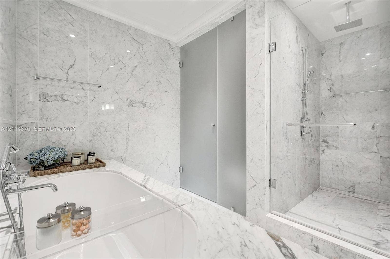 Sunny Isles Beach, Sunny Isles Beach, FL 33160 Floor-to-ceiling stone wall cladding, deep soaking tub with polished chrome deck-mounted faucet, and glass-enclosed walk-in shower featuring a rainfall showerhead and handheld wand
