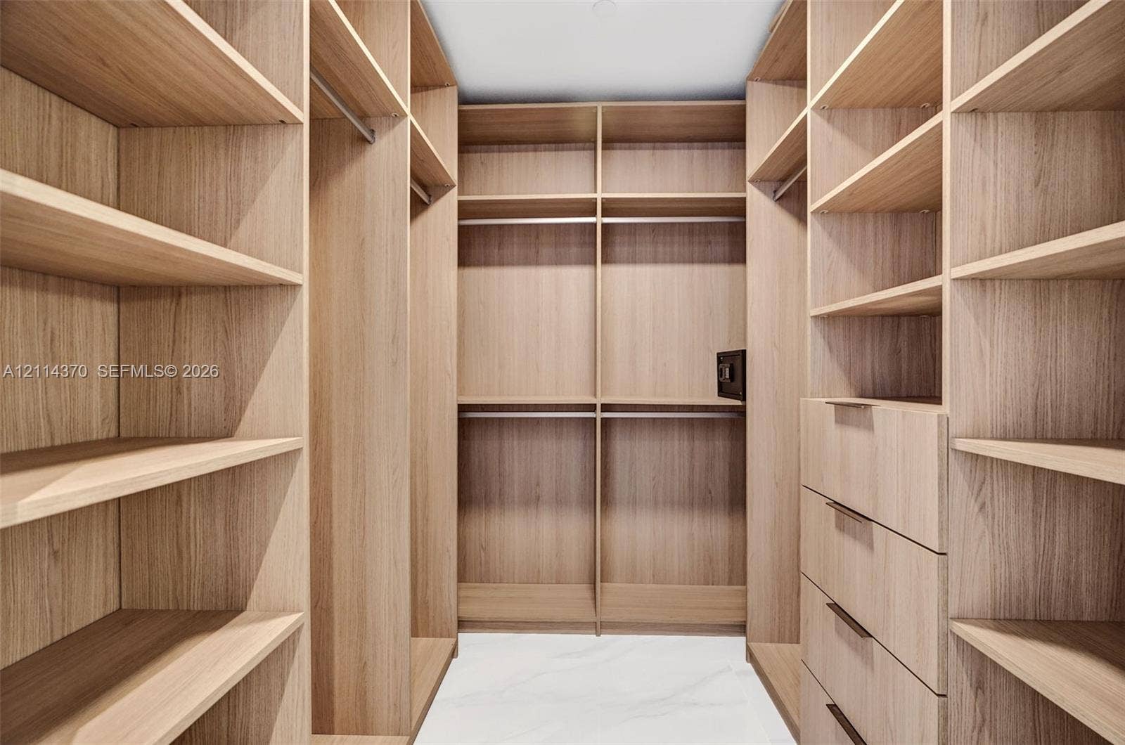 Sunny Isles Beach, Sunny Isles Beach, FL 33160 Custom walk-in closet featuring extensive wood-finish shelving, integrated clothing rods, a built-in safe, and a column of four drawers with matte hardware
