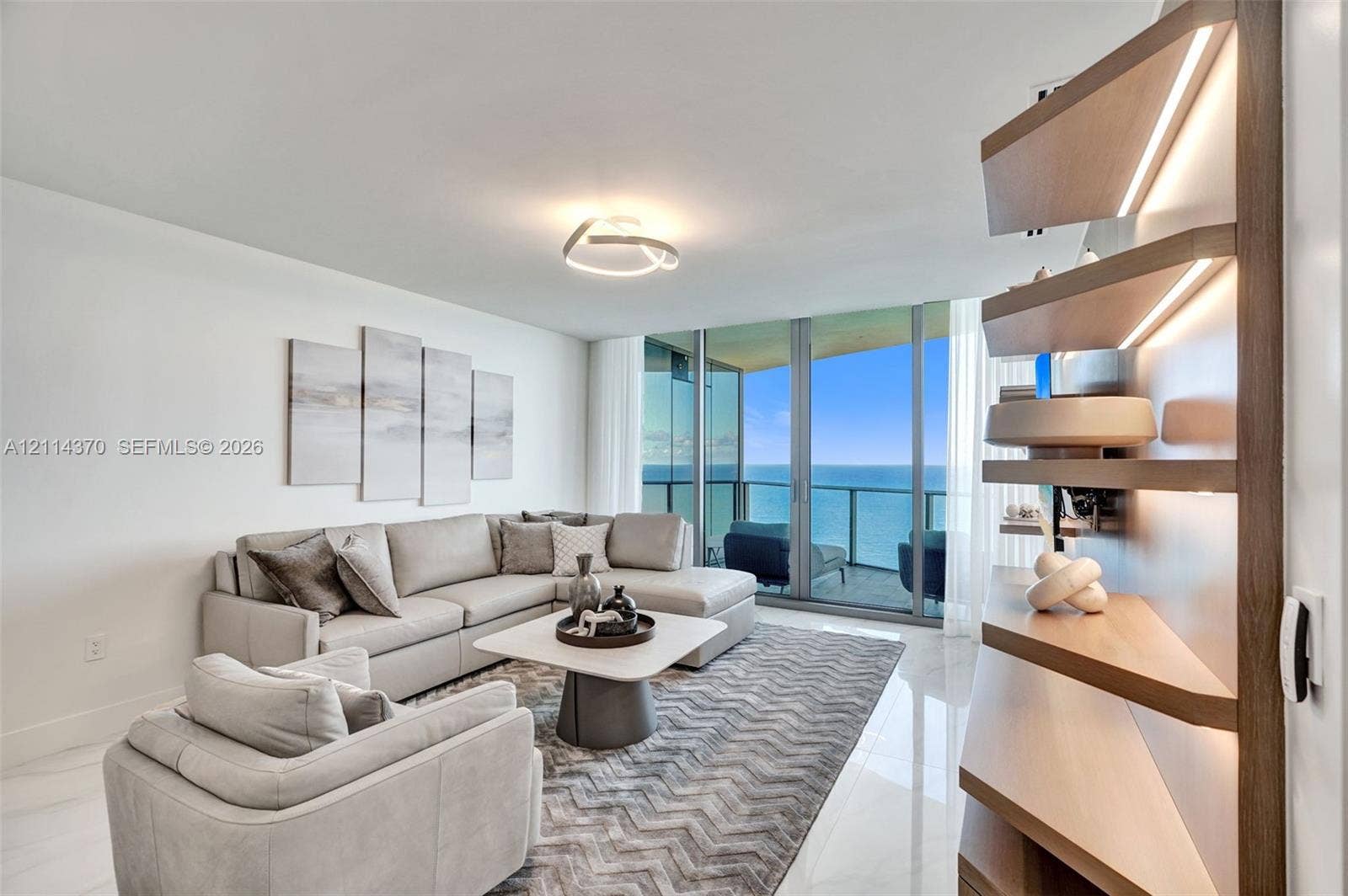 Sunny Isles Beach, Sunny Isles Beach, FL 33160 Floor-to-ceiling glass sliding doors with access to a balcony, built-in recessed wood-finish shelving with integrated LED lighting, and polished stone-finish flooring