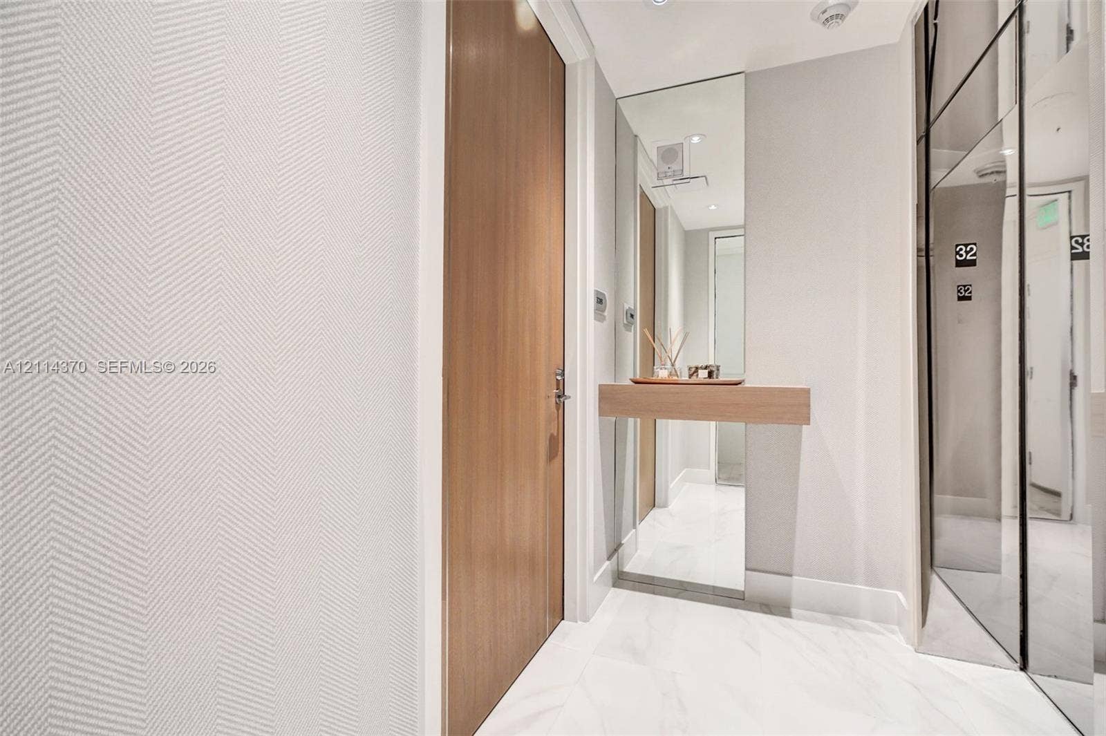 Sunny Isles Beach, Sunny Isles Beach, FL 33160 Textured chevron-patterned wall covering, full-height mirrored wall panel, stone-finish flooring, wood-veneer door, and floating wood-finish console shelf