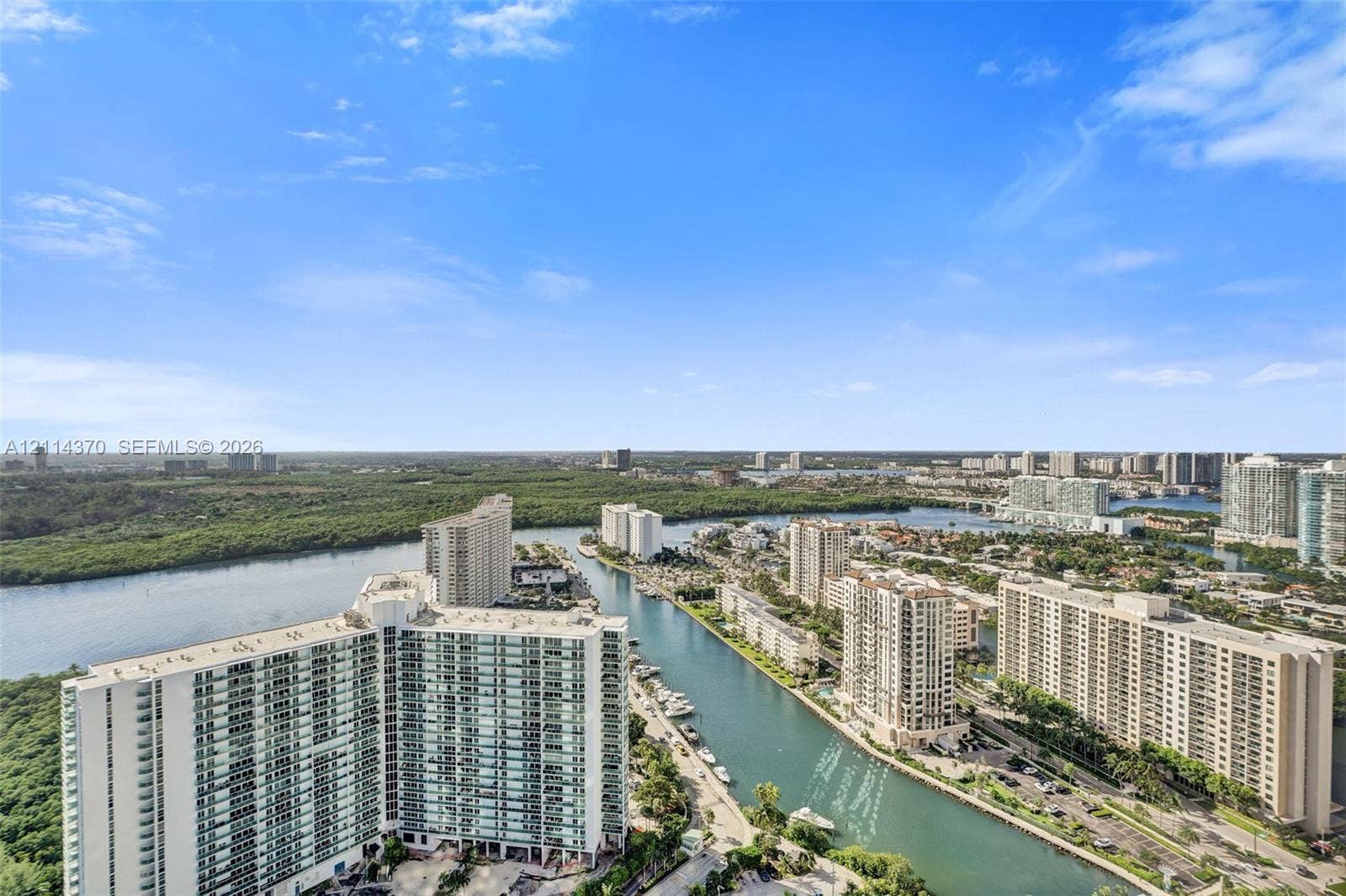 Sunny Isles Beach, Sunny Isles Beach, FL 33160 Panoramic coastal landscape featuring a waterway, high-rise residential buildings, and dense natural foliage under a clear sky