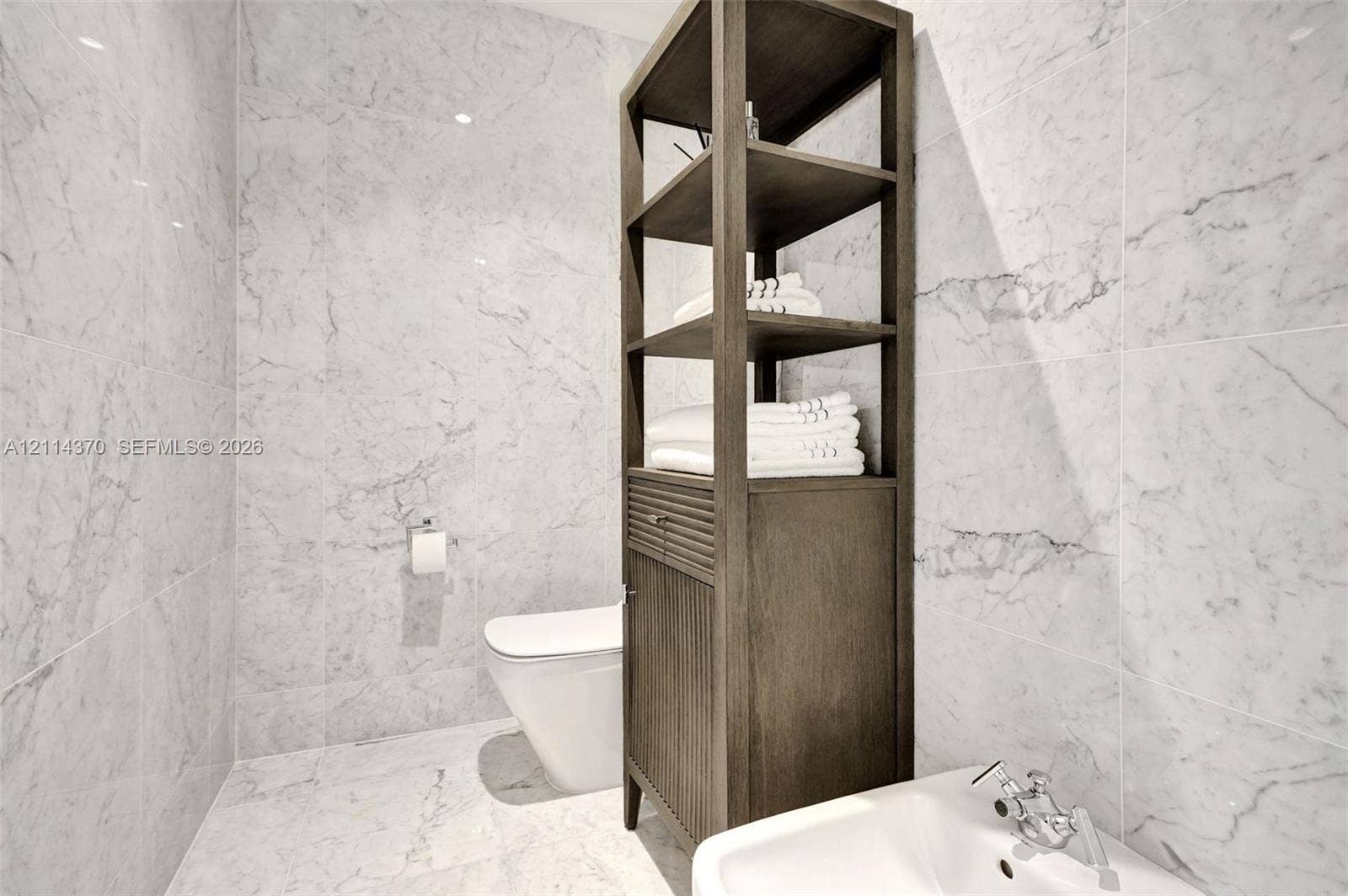 Sunny Isles Beach, Sunny Isles Beach, FL 33160 Full-height stone wall tiling, white wall-mounted toilet, custom dark wood built-in shelving unit with lower cabinetry, and wall-mounted basin