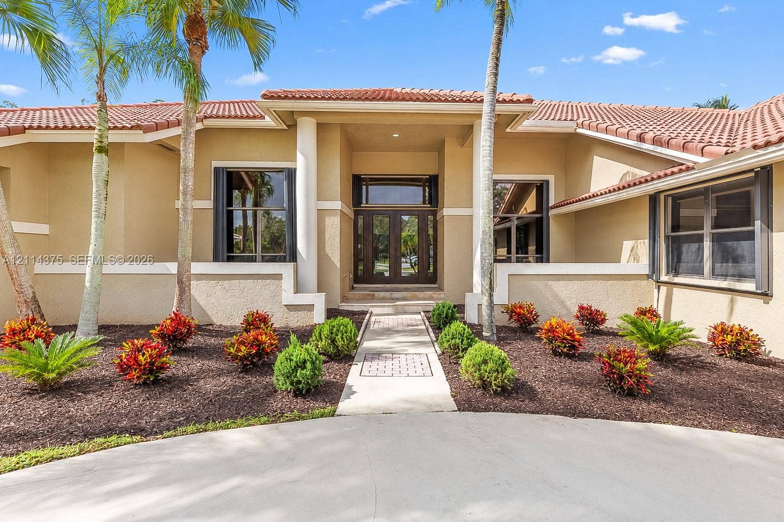 1206 S Manor Drive S, Weston, Weston, FL 33326 Stucco exterior featuring a terracotta tile roof, central recessed entryway with dual glass-paneled doors, decorative column accents, and a paved walkway