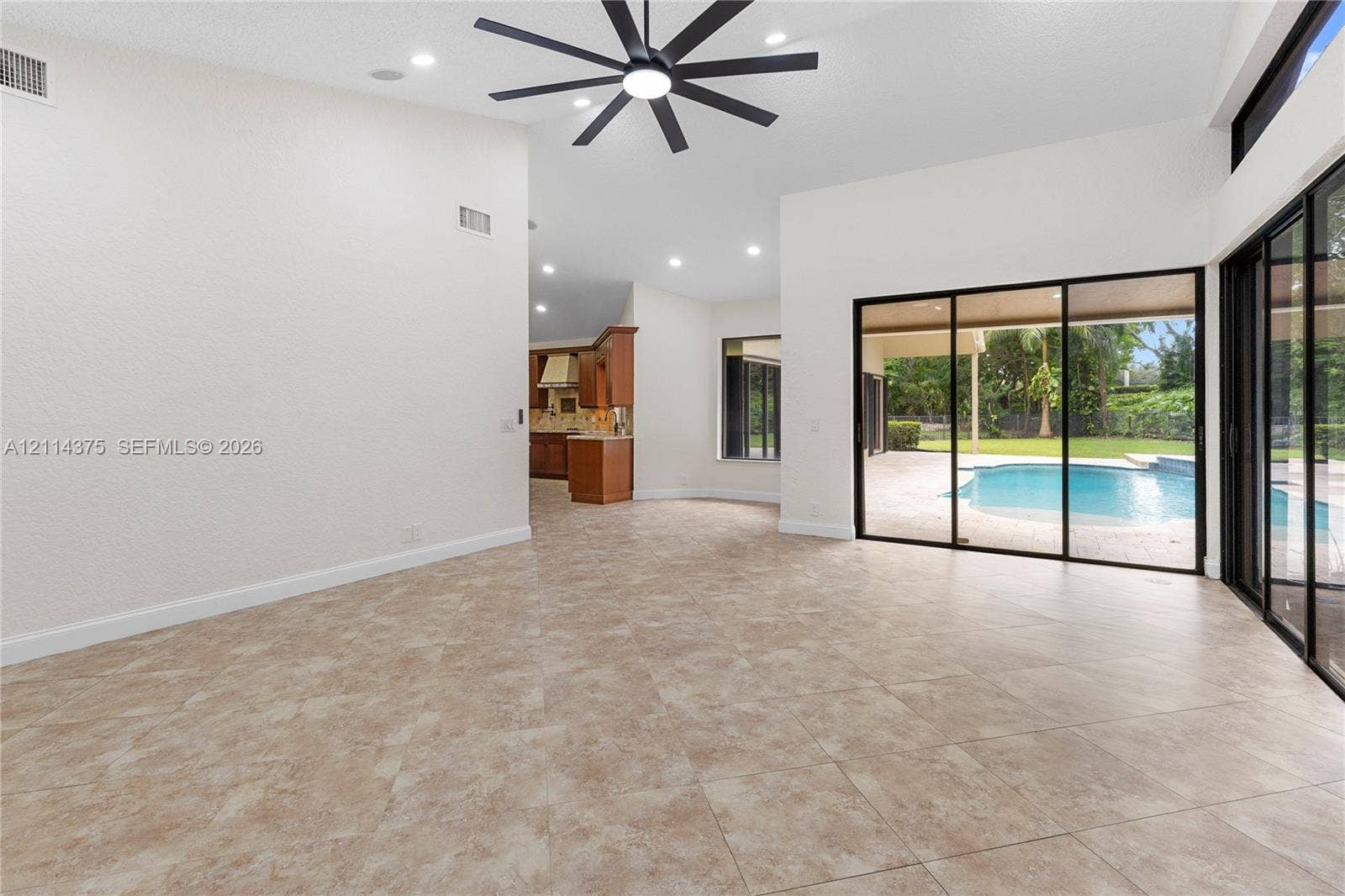 1206 S Manor Drive S, Weston, Weston, FL 33326 High ceilings with a multi-blade ceiling fan, large-format tile flooring, and expansive sliding glass doors opening to a private pool