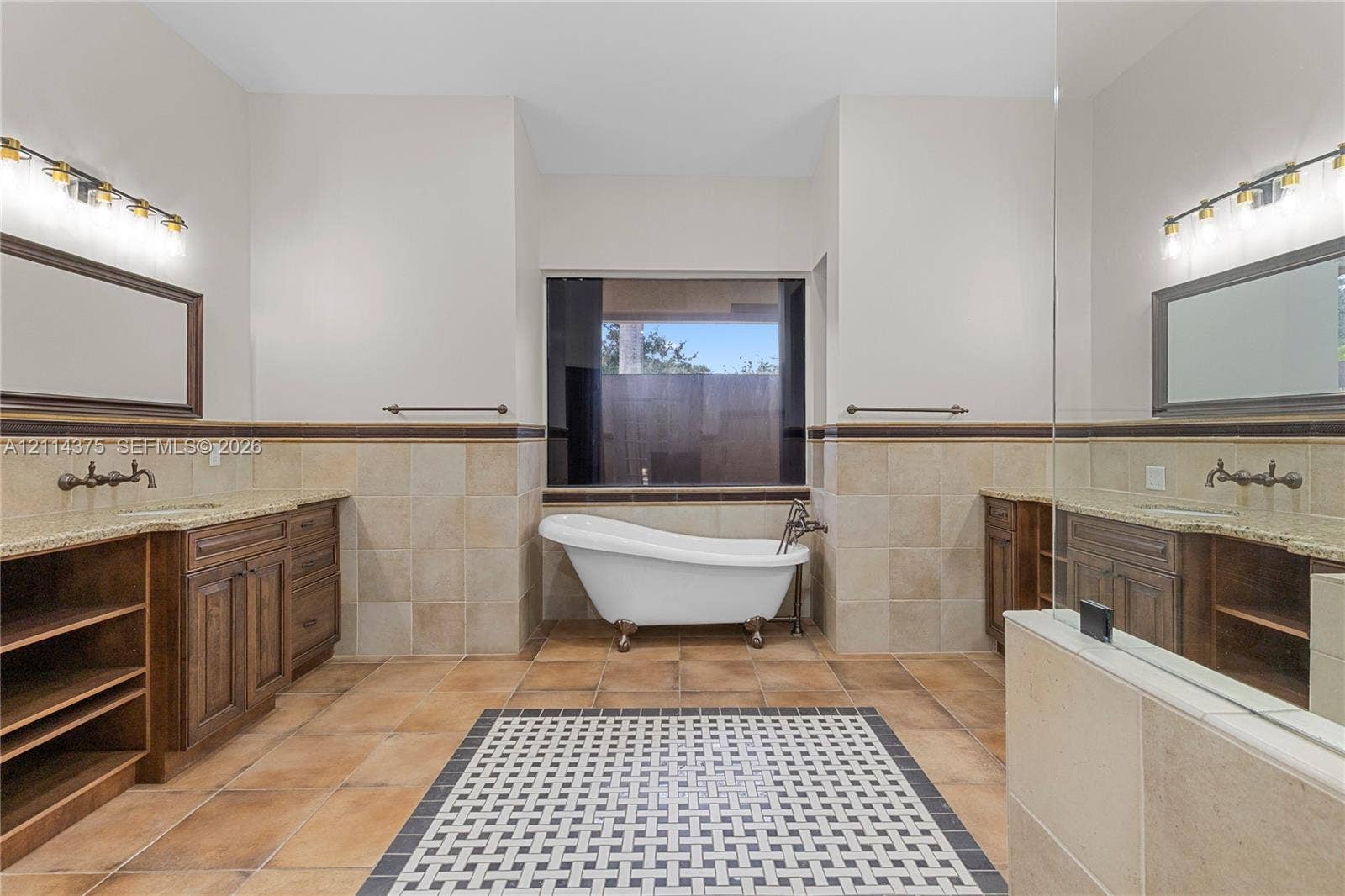 1206 S Manor Drive S, Weston, Weston, FL 33326 Freestanding clawfoot tub, dual wooden vanity cabinetry with stone countertops, decorative tile floor inlay, and wall-mounted vanity lighting